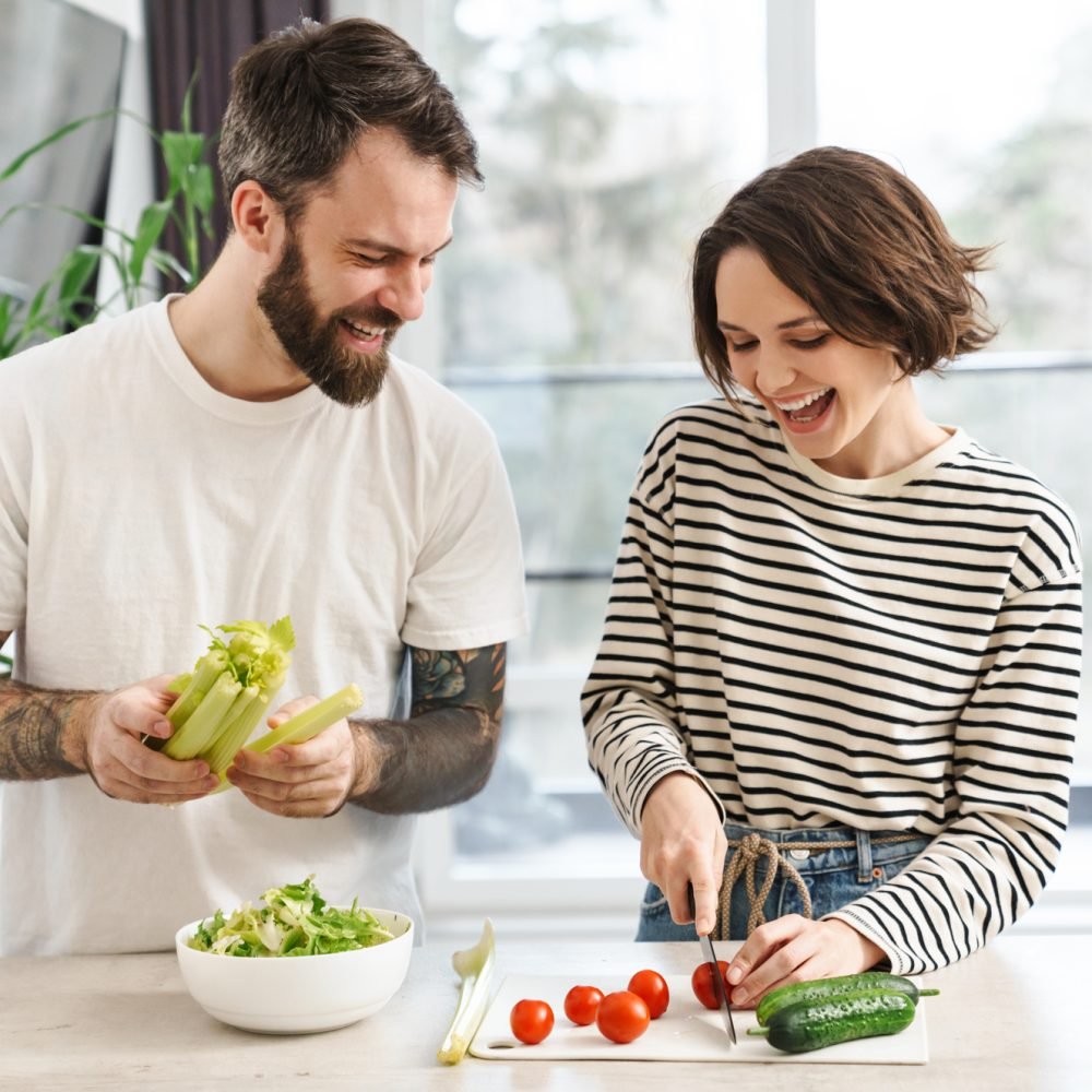 Young happy white couple cooking salad together in the kitchen at home